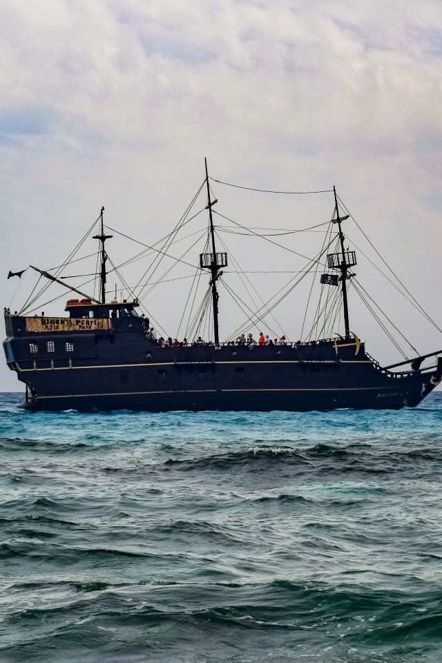 Large black pirate ship with lowered sails at sea