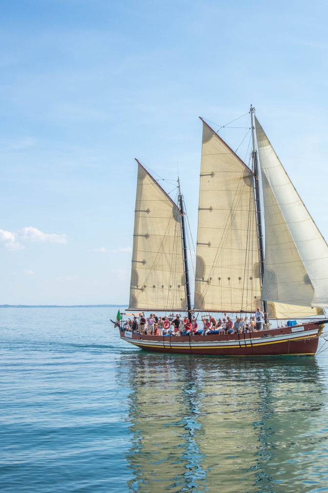 Судно с белыми парусами в море на фоне голубого неба 