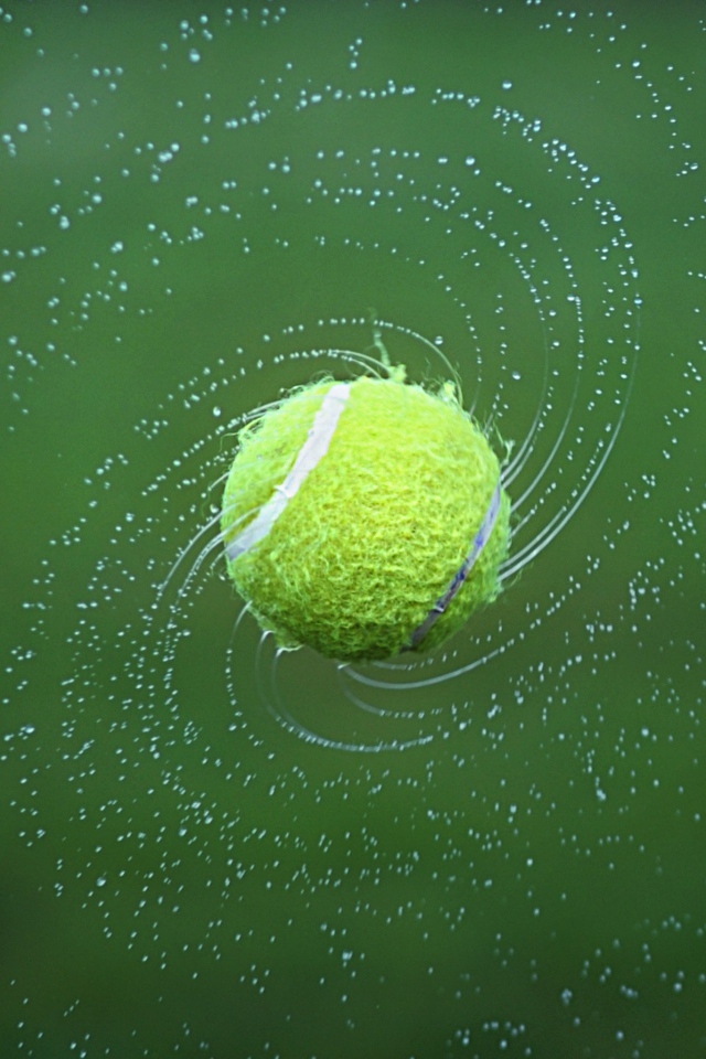 Теннисный мяч в брызгах воды на зеленом фоне
