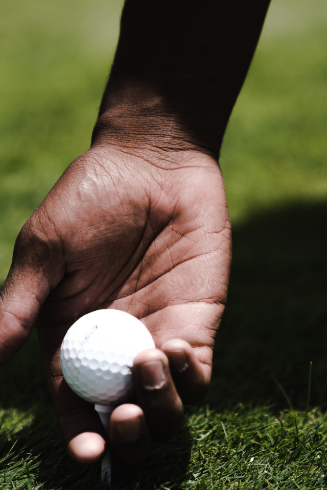 Белый мячик для гольфа в руке у мужчины на поле 