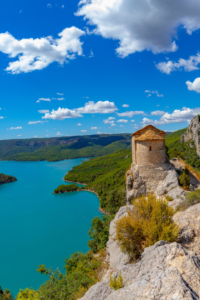 Старое здание на вершине утеса на фоне реки под голубым небом, Испания 