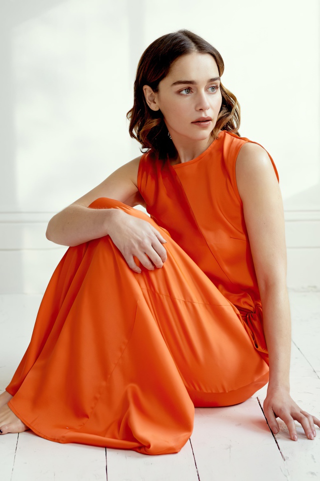 Актриса Эмилия Кларк  в оранжевом платье сидит на полу