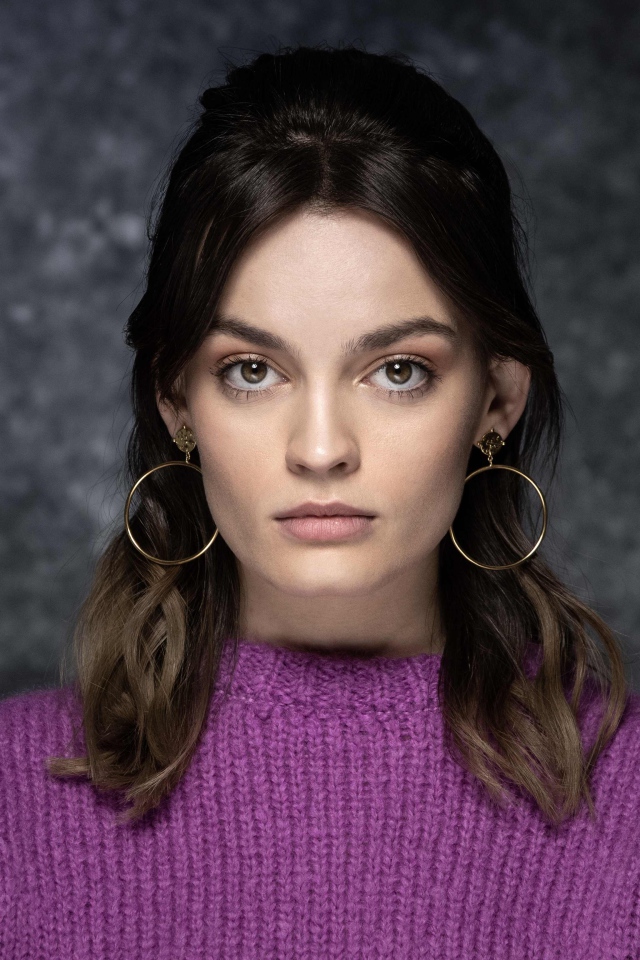 Актриса Эмма Маккей в сиреневом свитере на сером фоне