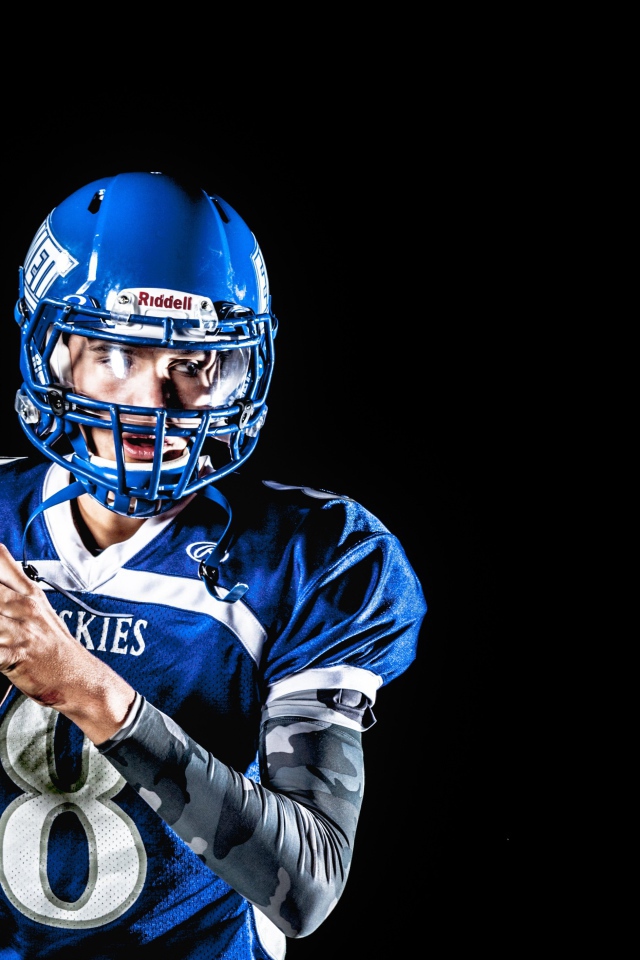 Игрок в американский футбол с мячом в руках на черном фоне 