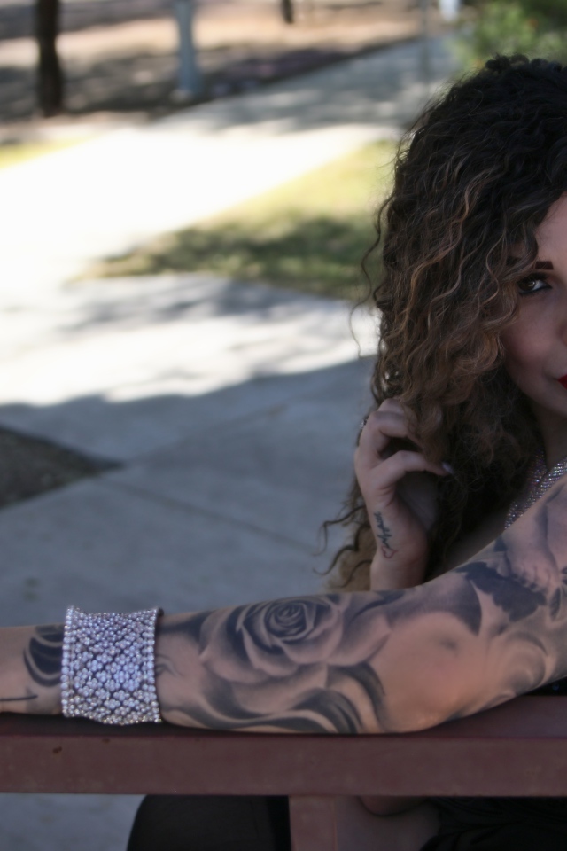 Beautiful girl with tattoos on her arms sits on a bench