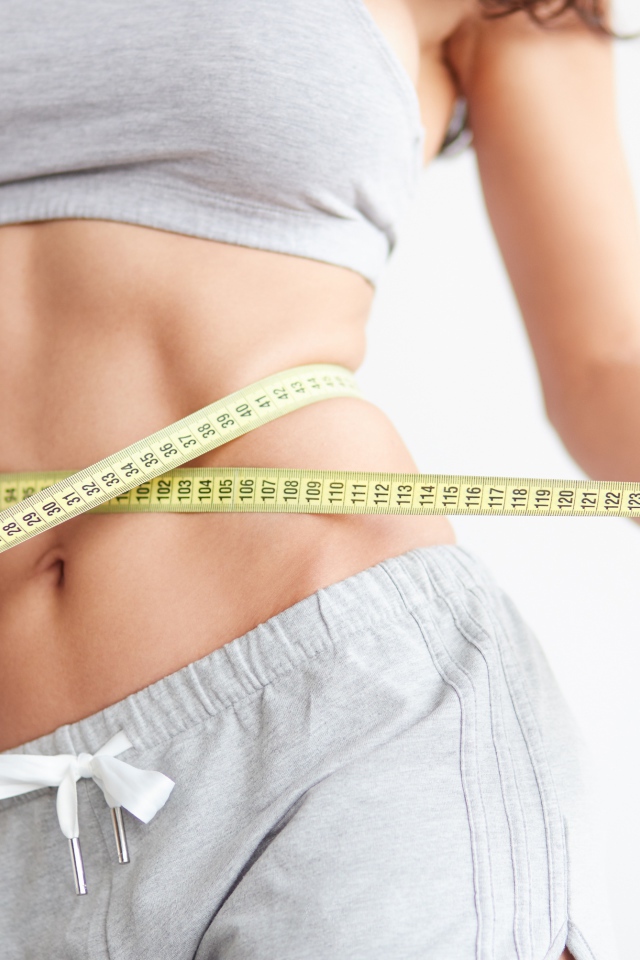 Красивая стройная девушка меряет талию сантиметром 