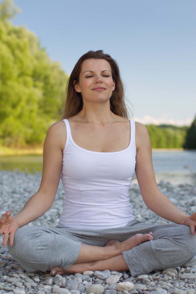 Девушка в позе лотоса медитирует у реки 
