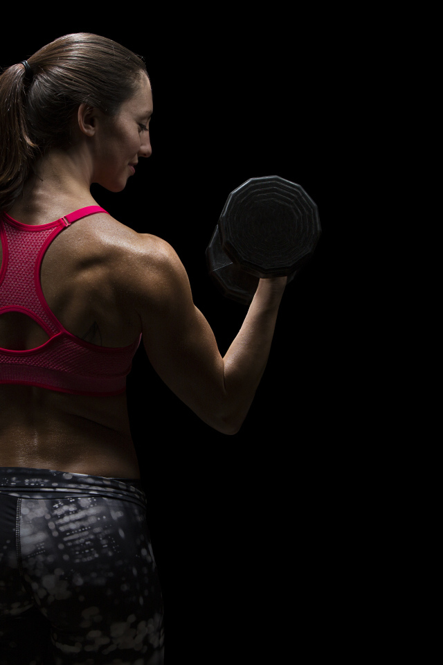 Девушка качает руки гантелей на черном фоне 