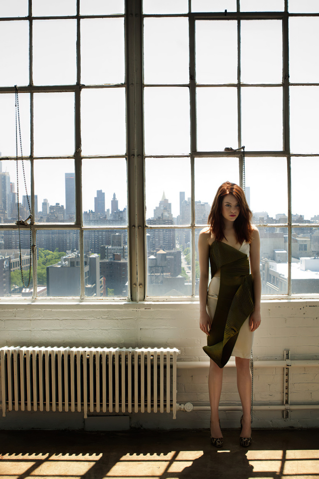 Популярная актриса Эмма Стоун стоит у большого окна