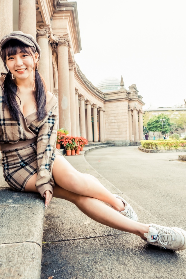 Улыбающаяся азиатка в кепке сидит на ступеньках 