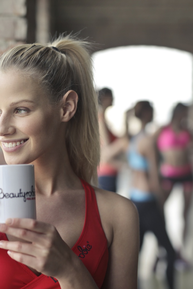 Улыбающаяся спортивная девушка с чашкой кофе у окна