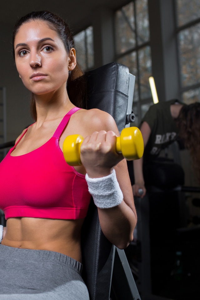 Спортивная девушка качает руки желтыми гантелями в спортзале
