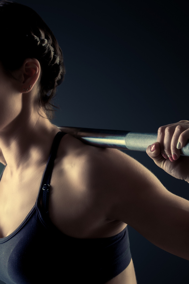 Спортивная девушка занимается со штангой в спортзале на сером фоне