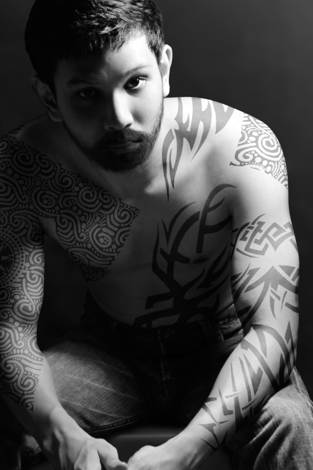 Молодой парень с татуировками на теле на сером фоне