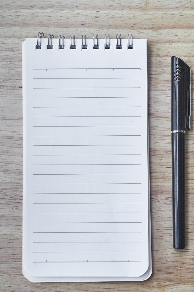 Авторучка и блокнот лежат на деревянном столе