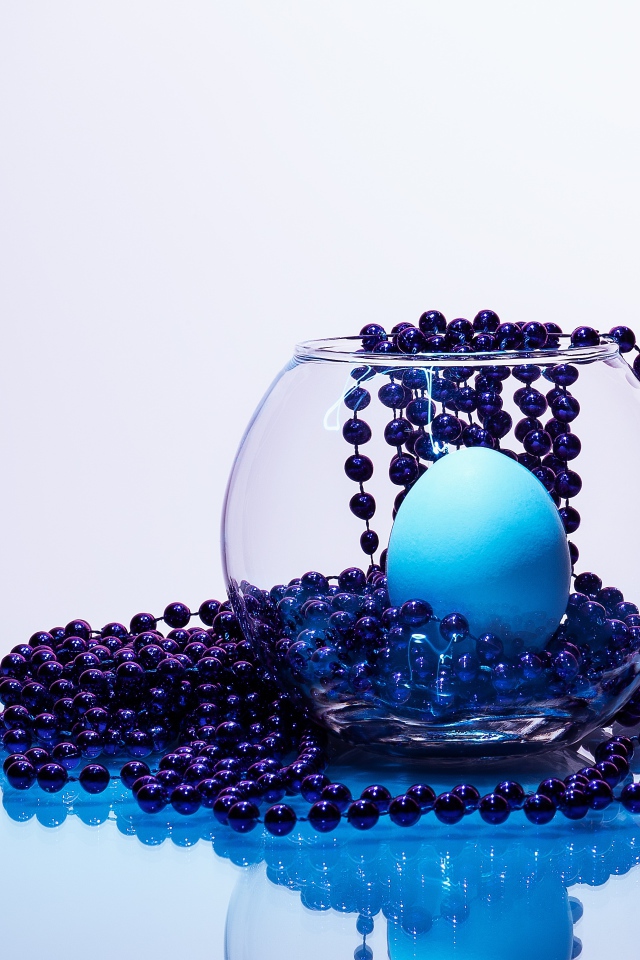 Синие бусы на столе со стеклянной вазой и яйцом