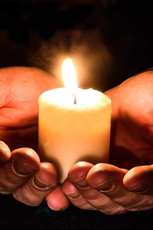 Зажженная свеча в руках на черном фоне