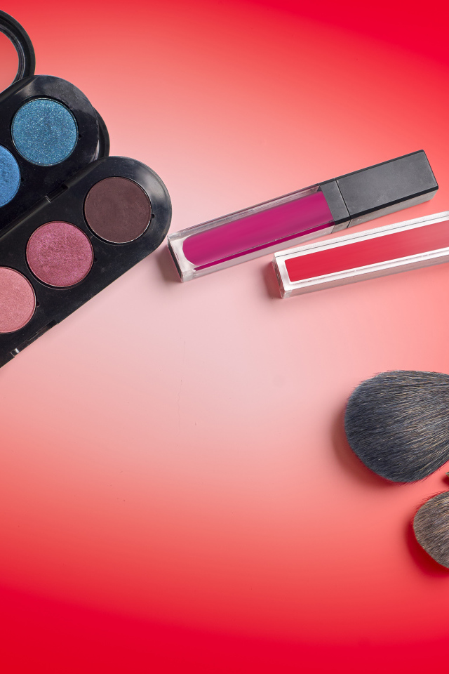 Блеск для губ, тени и кисточки на красном фоне