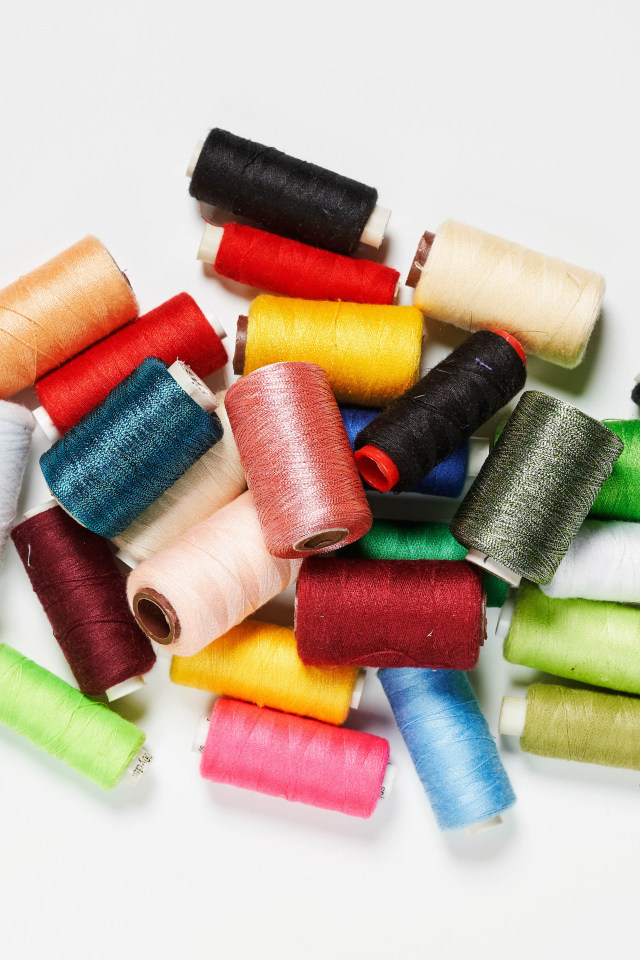 Много катушек разноцветных ниток на белом фоне 