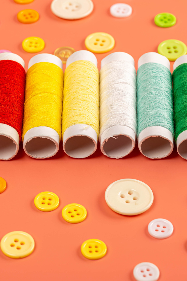 Разноцветные нитки и пуговицы на розовом фоне