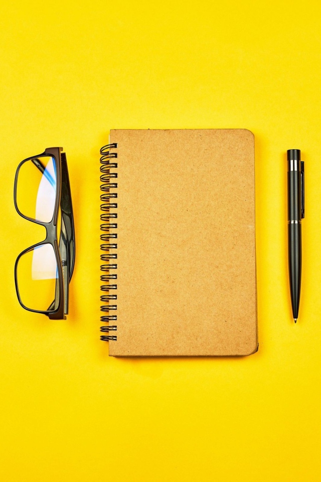 Блокнот, очки и ручка на желтом фоне