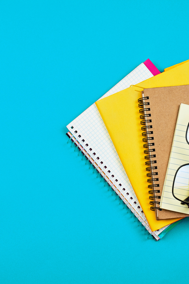 Блокноты, очки и ручка на голубом фоне