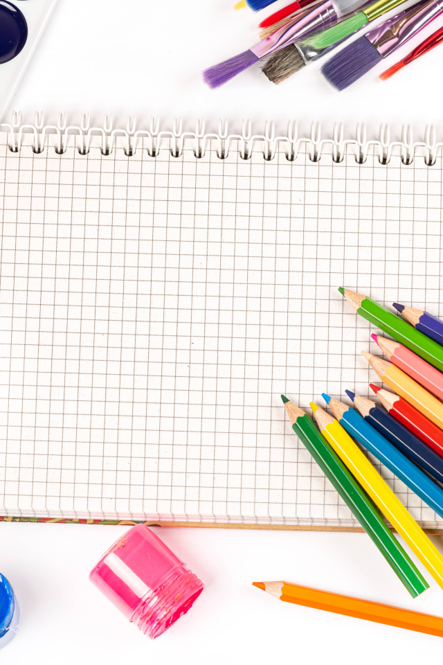 Карандаши, краски и тетрадь на белом фоне 