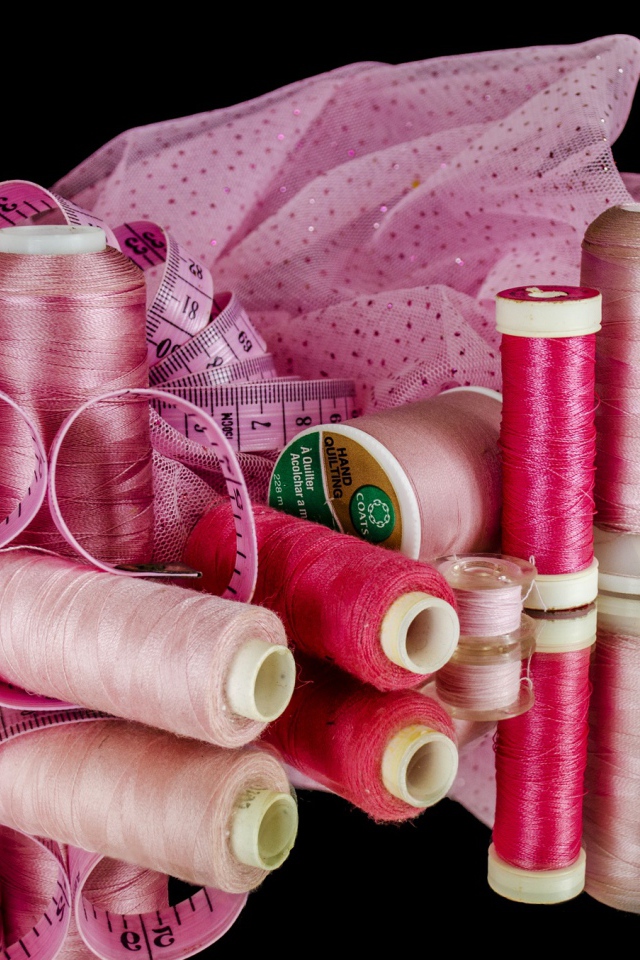 Розовые нитки с сантиметром и тканью на черном фоне 