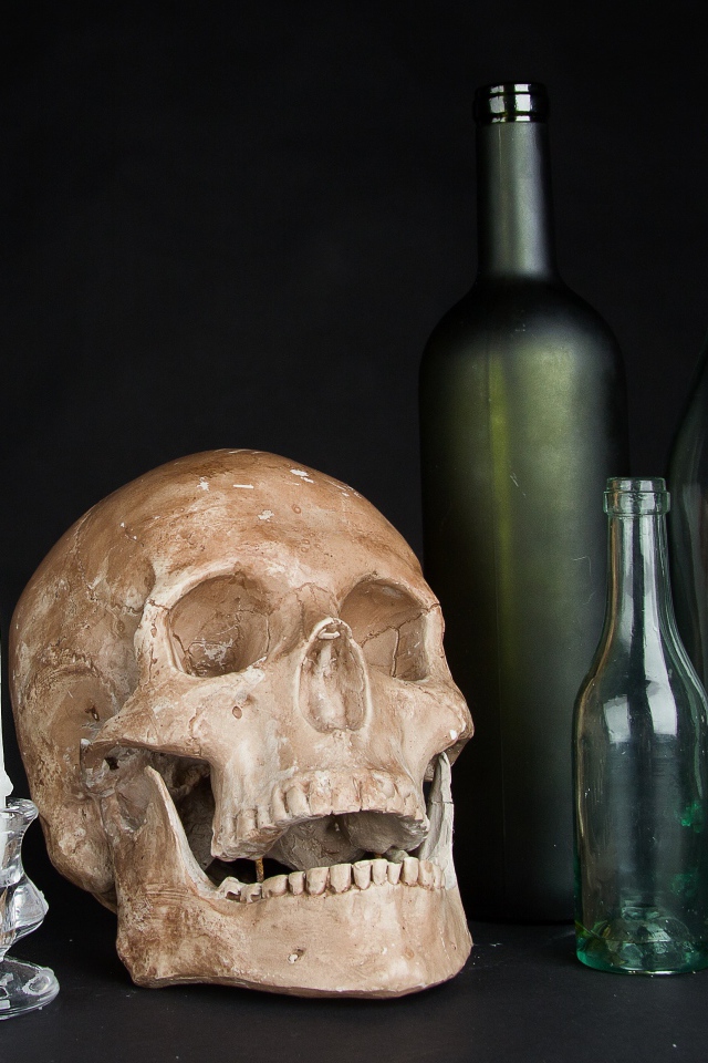 Череп, пустые бутылки и свеча на черном фоне