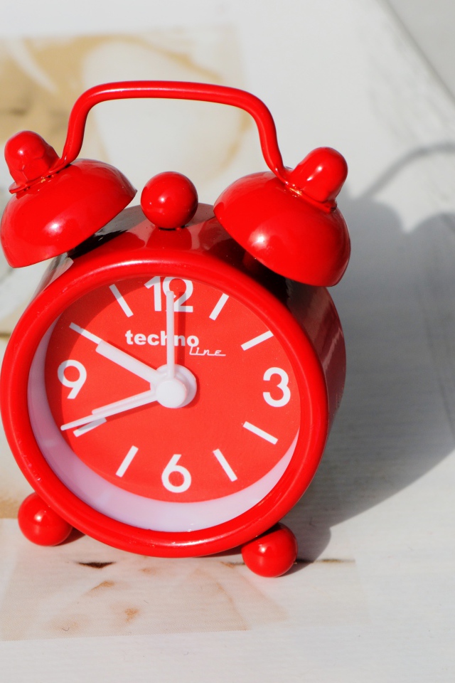 Маленький красный будильник стоит на столе 