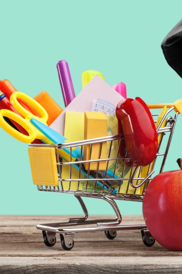 Канцелярские предметы в тележке на столе с яблоком и книгами 