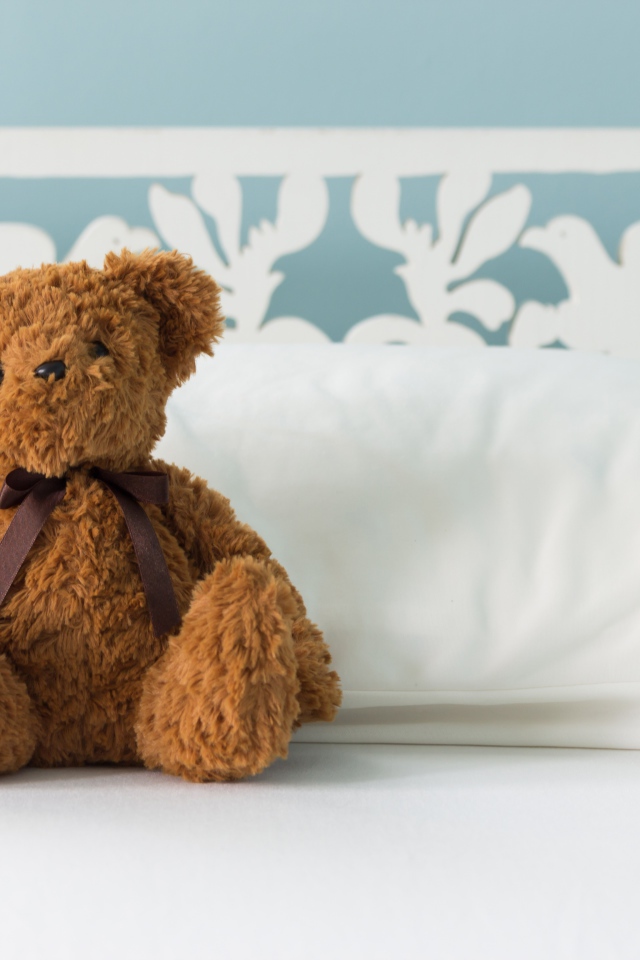 Игрушечный медвежонок сидит на белой постели