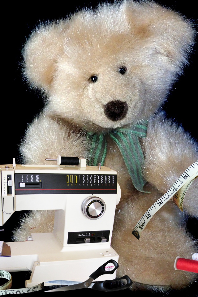 Игрушечный медвежонок со швейной машинкой на черном фоне 