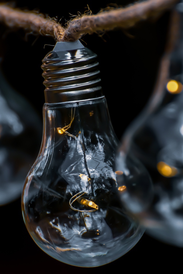 Три лампочки висят на веревке на черном фоне