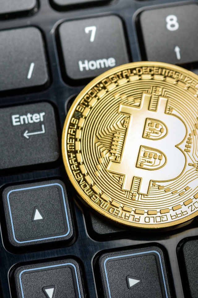 Золотая монета биткоин на черной клавиатуре