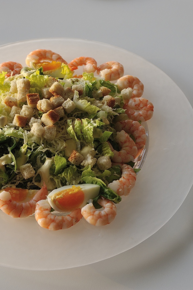 Тарелка аппетитного салата с креветками на столе с рюмкой