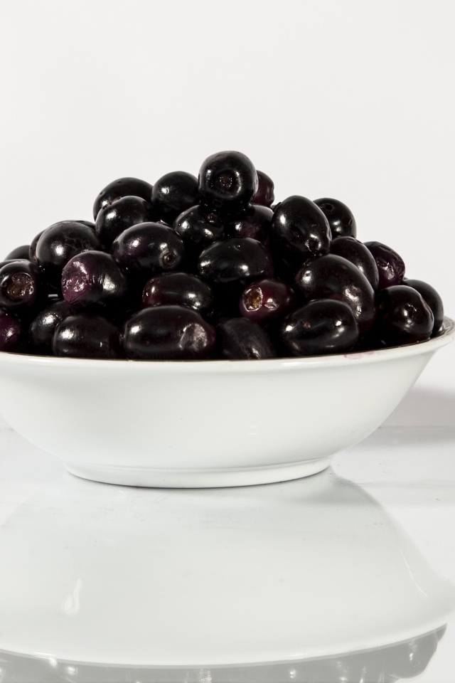 Черные оливки в белой тарелке отражаются в поверхности