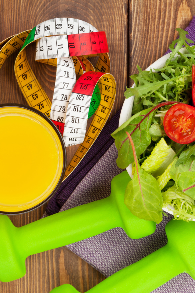 Салат из зелени на столе с соком и гантелями