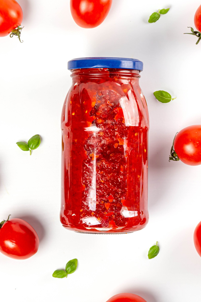 Банка аджики на белом фоне с помидорами