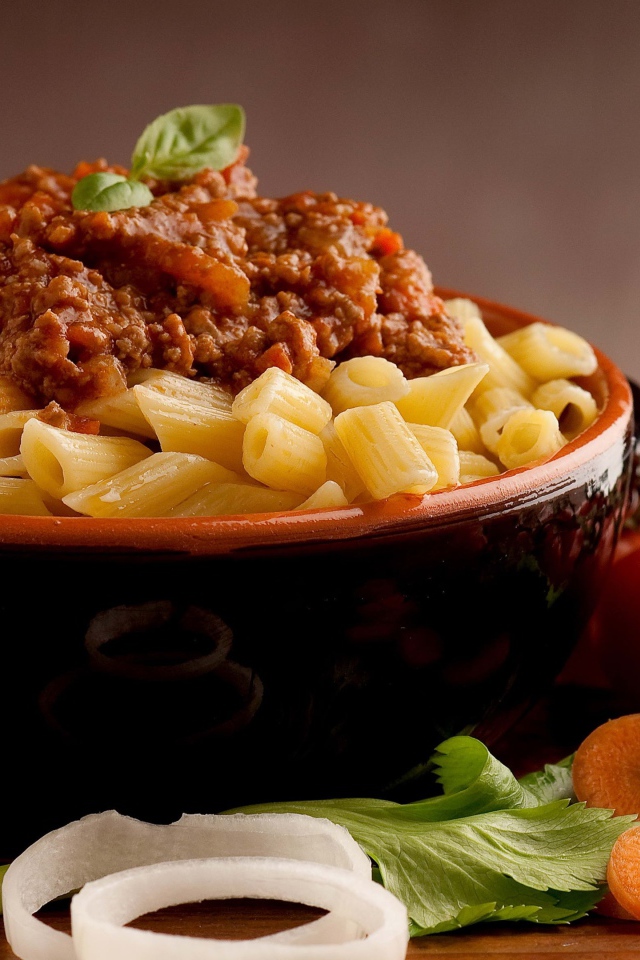 Макароны в миске с фаршем на столе с помидорами