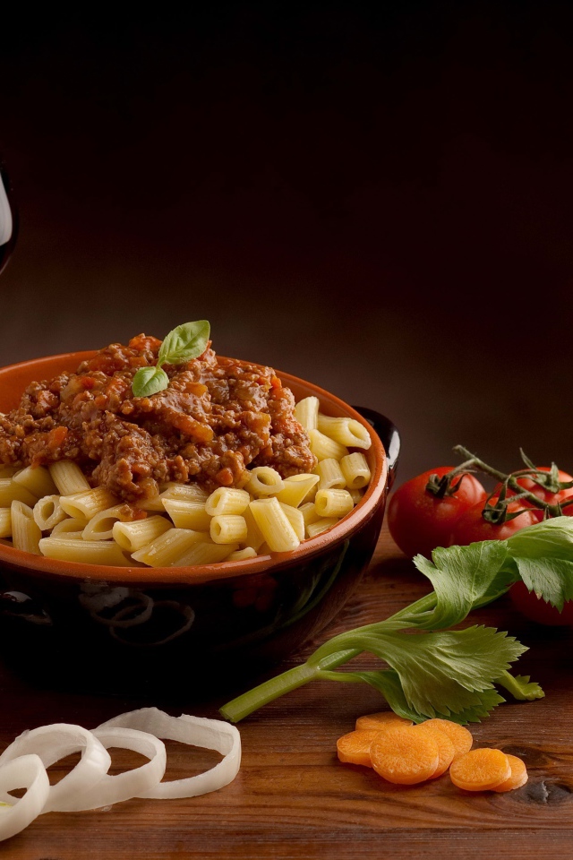 Макароны с фаршем на столе с бокалом вина и помидорами