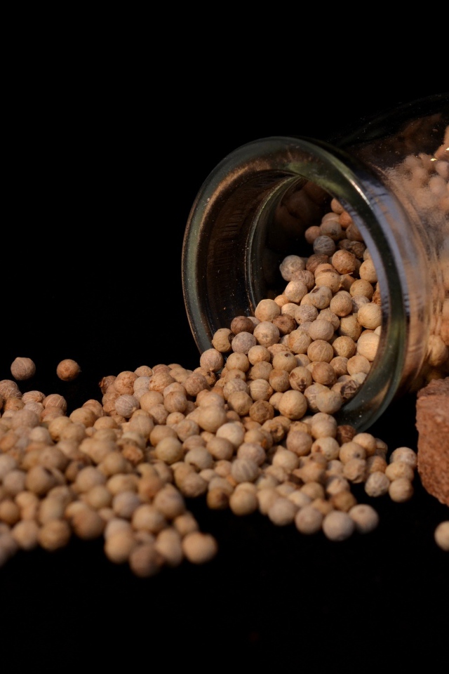 Перец горошек в стеклянной банке на черном фоне 