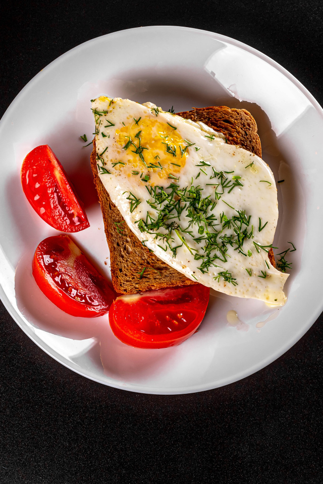 Кусок хлеба с яичницей на тарелке с помидорами