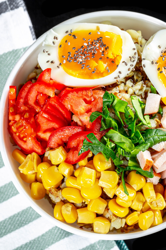 Каша в тарелке с помидорами, кукурузой, ветчиной и яйцом