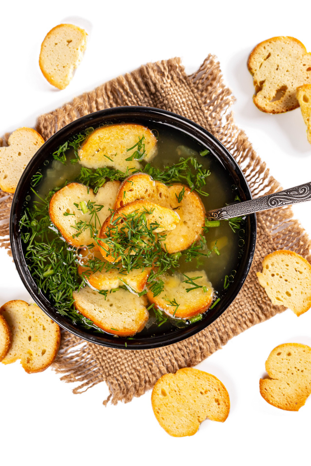 Суп с гренками и зеленью на столе на белом фоне