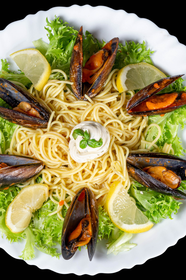 Спагетти с мидиями и листьями салата на белой тарелке