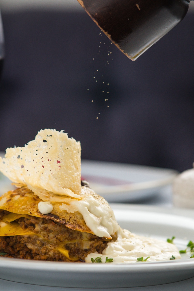 Кусок лазаньи посыпают перцем 