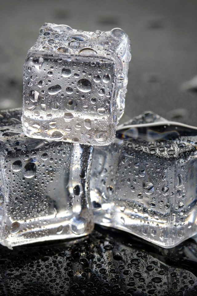 Три кусочка льда в брызгах воды на столе 