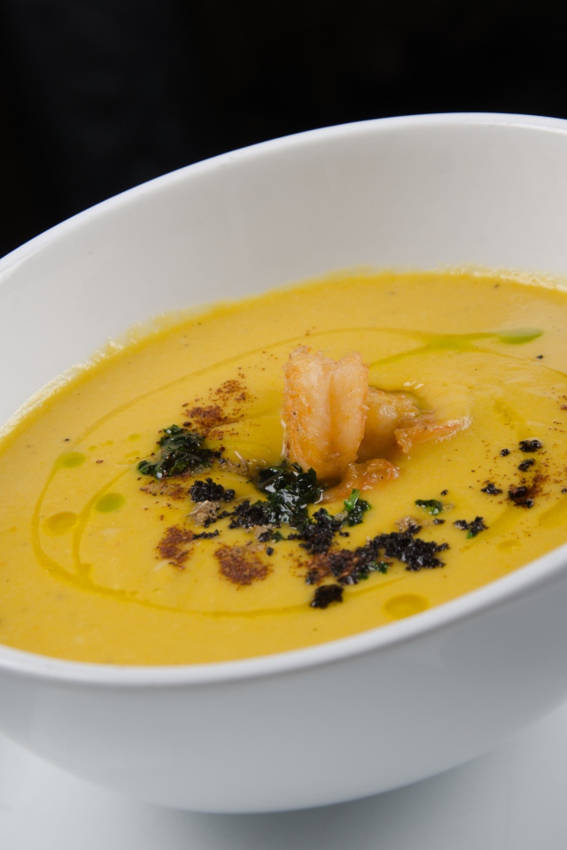 Желтый суп пюре в белой тарелке на черном фоне