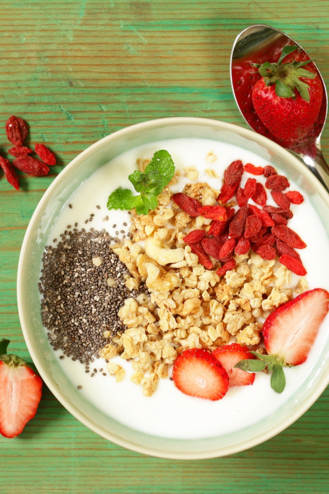 Йогурт с сухофруктами и клубникой на столе в миске 